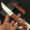 A man's hand holding a Tanto folding knife on his fingertips.