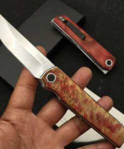 A man's hand holding a Tanto folding knife on his fingertips.