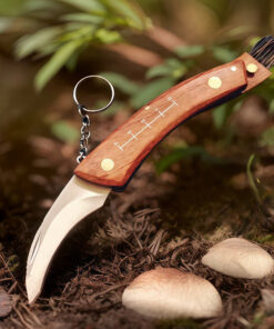 A mushroom knife with brush, displayed against a forest floor background.