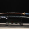 A red blade Katana sword, displayed on a small wooden stand, alongside its scabbard.