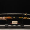 A folded steel sword Katana, displayed on a small wooden stand, alongside its scabbard.