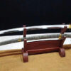 A hand forged Tamahagane Katana, displayed on a woden stand, alongside its scabbard.